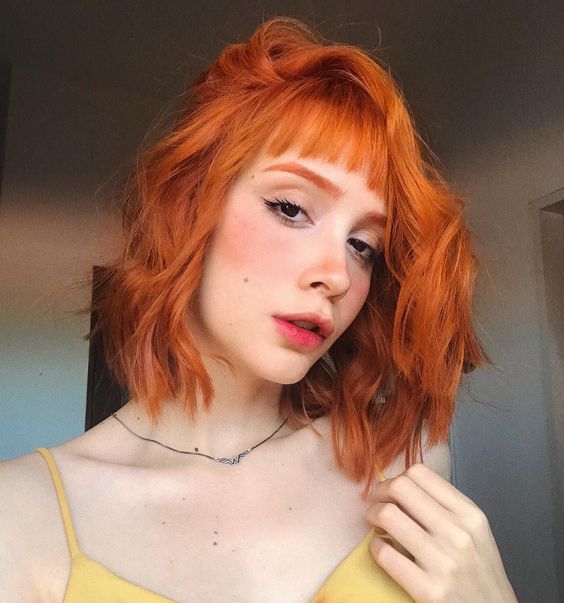 a long wavy ginger red bob with a classic fringe is a cool and bright solution that makes a statement with color