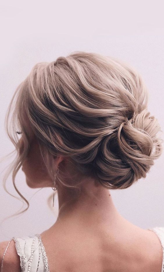 a loose low bun of wavy hair, wiht a wavy and voluminous top and face framing is a cool idea for an elegant bride
