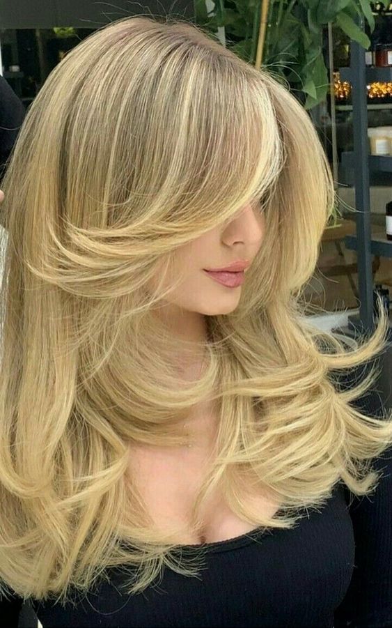 a lovely golden blonde butterfly haircut with wavy ends and a lot of volume is a catchy and chic idea