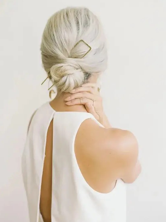 a low bun with a bump and an oversized gilded accessory is ideal for a minimalist bride
