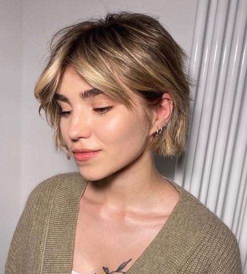 A messy and shaggy jaw length bob with blonde balayage and short curtain bangs plus waves is a very fresh solution