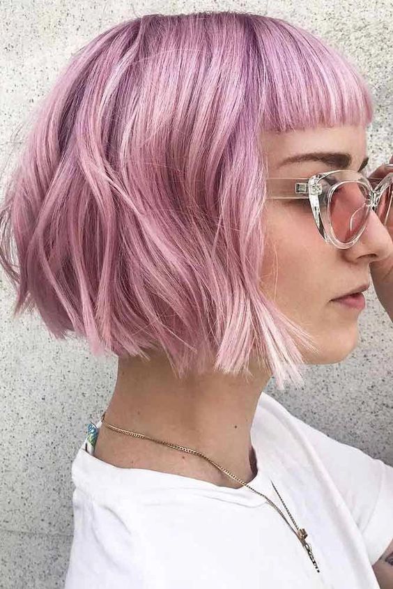 A pink chin length bob with baby bangs and waves plus volume is a bold and edgy idea