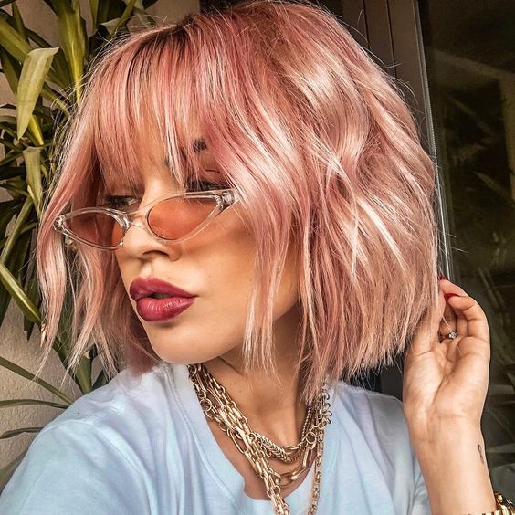 a pink midi length bob with outgrown wispy bangs and waves is a cool and chic idea