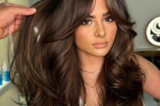 a rich brown long butterfly haircut with caramel balayage and bottleneck bangs with a lot of volume and waves