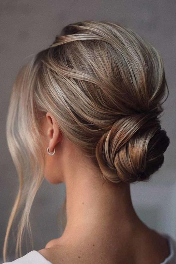 a simple twisted and wrapped low bun with a bump on top and some face framing locks is a cool idea for a modern and glam bride