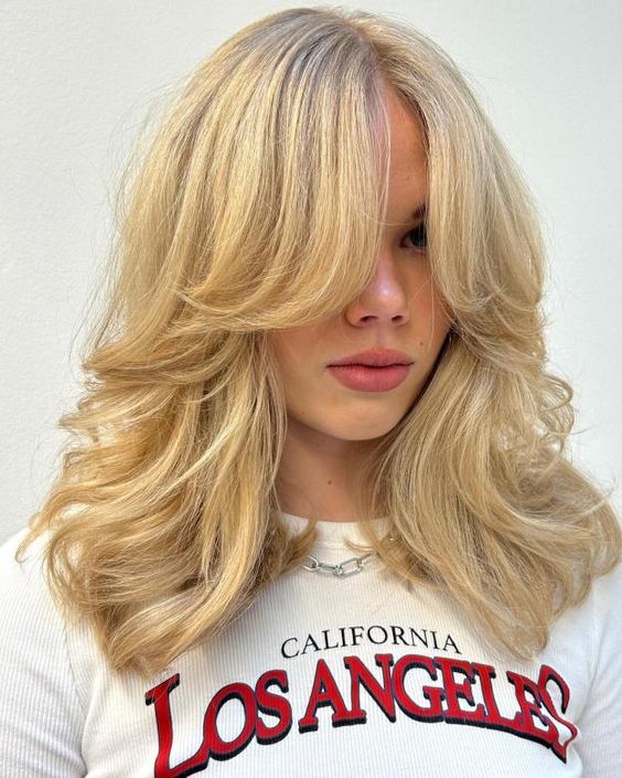 a stunning blonde butterfly haircut with curtain bangs and wavy ends plus a lot of volume is amazing and chic