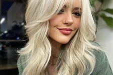a sunny blonde medium-length butterfly haircut with wispy bangs and a lot of volume is a chic and pretty idea to try