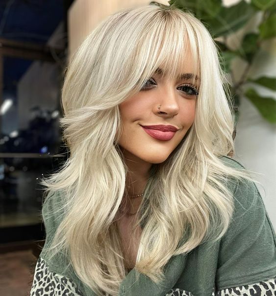 a sunny blonde medium-length butterfly haircut with wispy bangs and a lot of volume is a chic and pretty idea to try