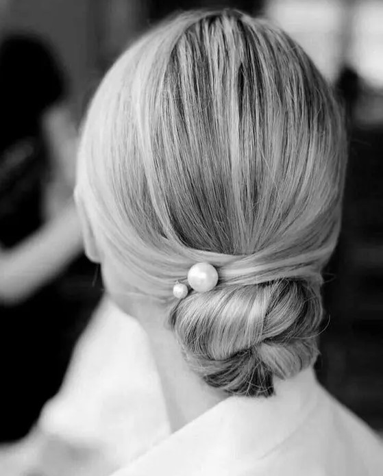 a super sleek low bun hairstyle with no bumps is spruced up with large pearl pins for a chic look
