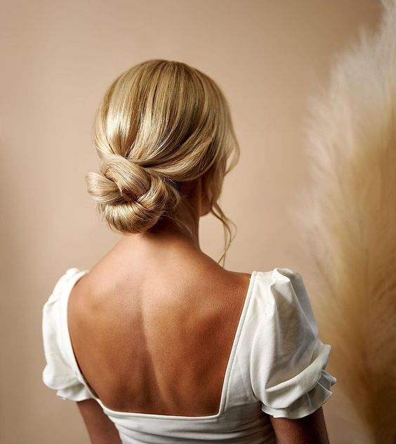 a twisted low bun with a sleek top and waves down is a stylish idea for a modern wedding, it looks chic and cool