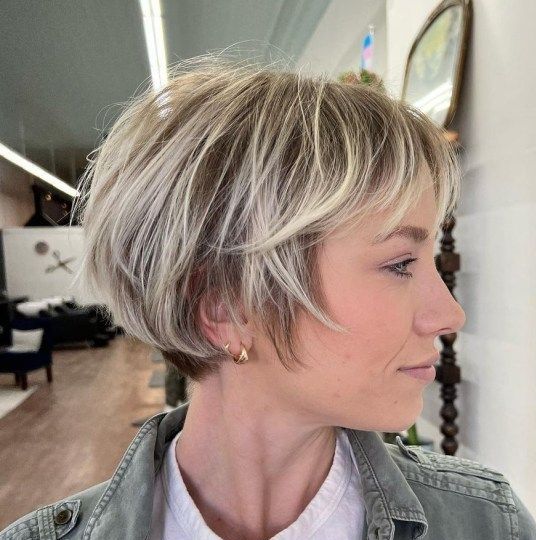 an ear length bob with blonde balayage and wispy bangs is a stylish and chic idea that looks airy