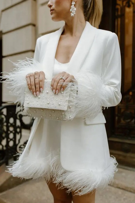a white mini dress with feathers, a white blazer with feathers on the sleeves, a pearl bag and earrings