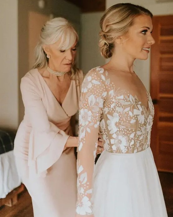 A blush fitting dress with a V neckline and bell sleeves plus pearls for a very chic and feminine mother of the bride look