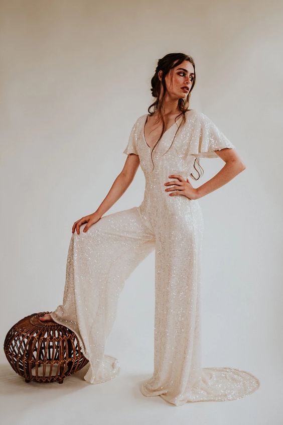 A shiny white sequin jumpsuit with a V neckline, short sleeves, wideleg pants with a train for a bridal party
