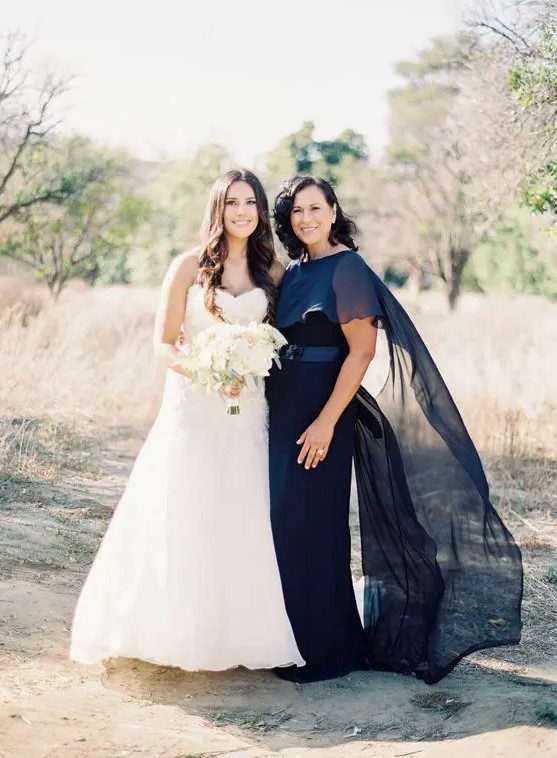 a navy maxi dress with a fitting silhouette, a sash and a sheer capelet on top are an amazing outfit for a formal wedding