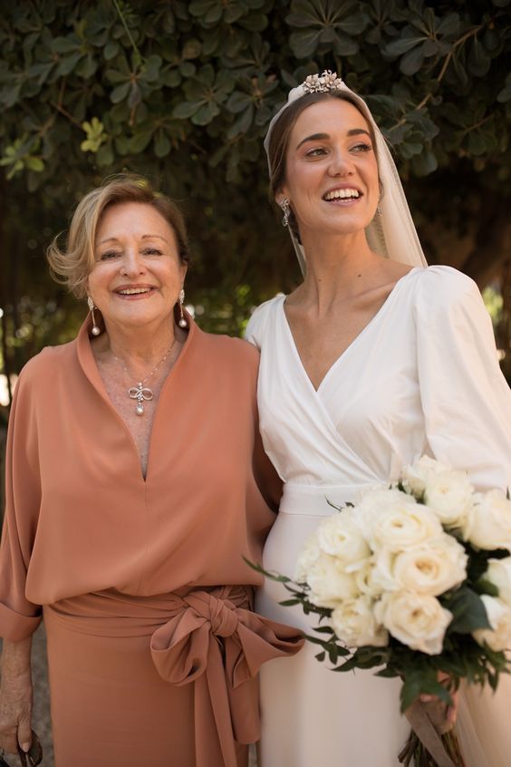 a plain terracotta dress with short sleeves, a deep neckline, a sash with a bow and statement accessories for the mother of the bride