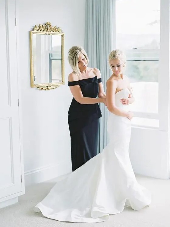an elegant black fitting off the shoulder dress with an oversized bow is very chic and bold for a mother of the bride
