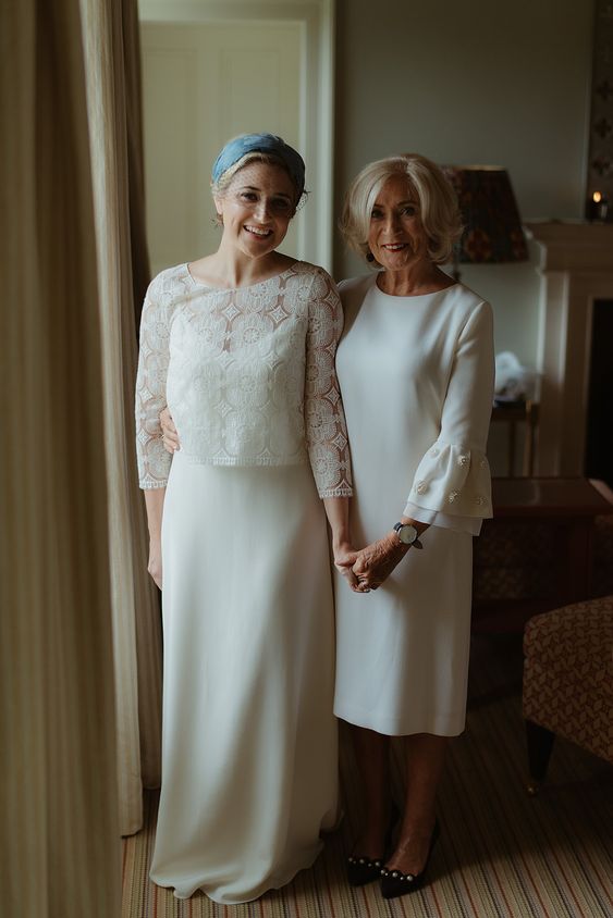 an elegant plain white midi dress with a high neckline, bell embellished sleeves and black embellished shoes for the mother of the bride