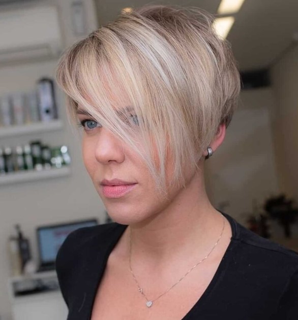 a beautiful blonde pixie haircut with icy highlights and long side bangs that can be worn either side