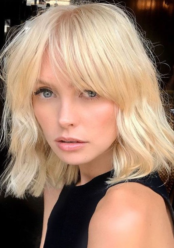 A blonde medium length haircut with bottleneck bangs and a bit of texture is a bold and cool idea