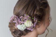 a braided halo with a bump on top and a low bun, fresh flowers tucked in is a chic and lovely idea for a flower girl
