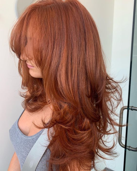 a bright and catchy red butterfly haircut with long wispy bangs, curled ends and a lot of volume really makes a statement