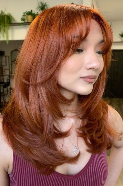 a copper butterfly haircut with bottleneck bangs and wavy ends plus a lot of volume is amazing