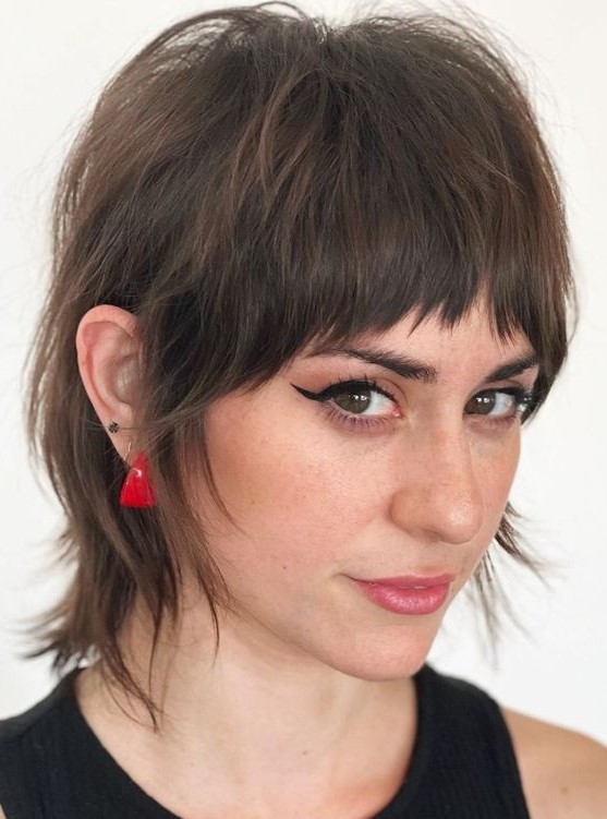 a dark brunette short pixie mullet with bangs, a dimensional crown and shaggy touches is a gorgeous haircut styled right