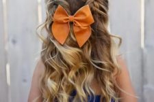 a half updo with braids on top and waves down, a bold orange bow for an accent is a very lovely and girlish idea