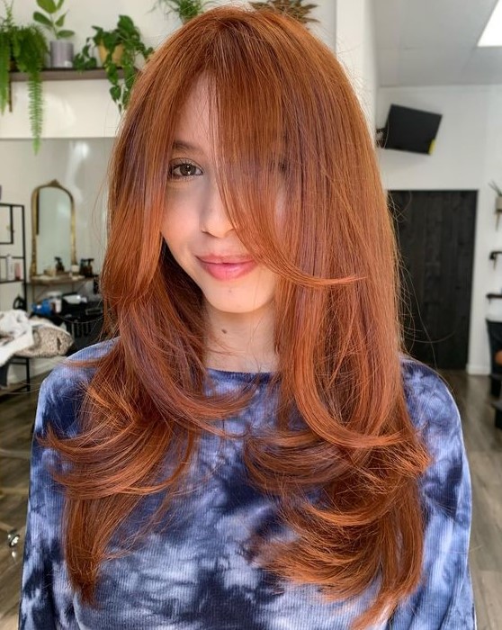a long and beautiful ginger butterfly haircut with curled ends and bottleneck bangs is a cool and bold idea