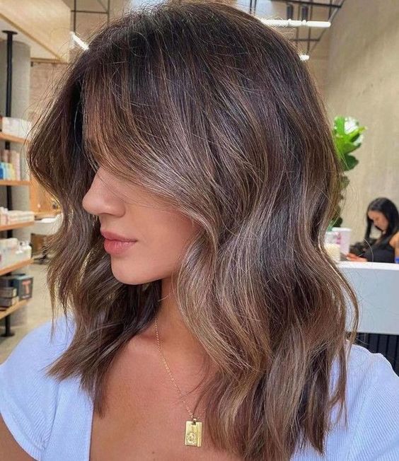 A lovely brunette medium length haircut with slight caramel contouring and highlights plus waves is very chic