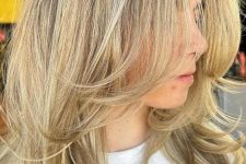 a medium-length blonde butterfly haircut with curled ends, a bit of volume and a darker root is a stylish idea