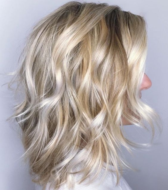 A medium length blonde shaggy haircut with a darker root, waves and volume is a very eye catching idea