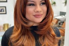 a pretty red to giner butterfly haircut with baby wispy bangs and a lot of volume, an ombre effect makes it bolder