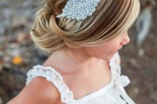 a refined flower girl hairstyle with a low bun and a bump, with a rhinestone headpiece is a chic and stylish idea