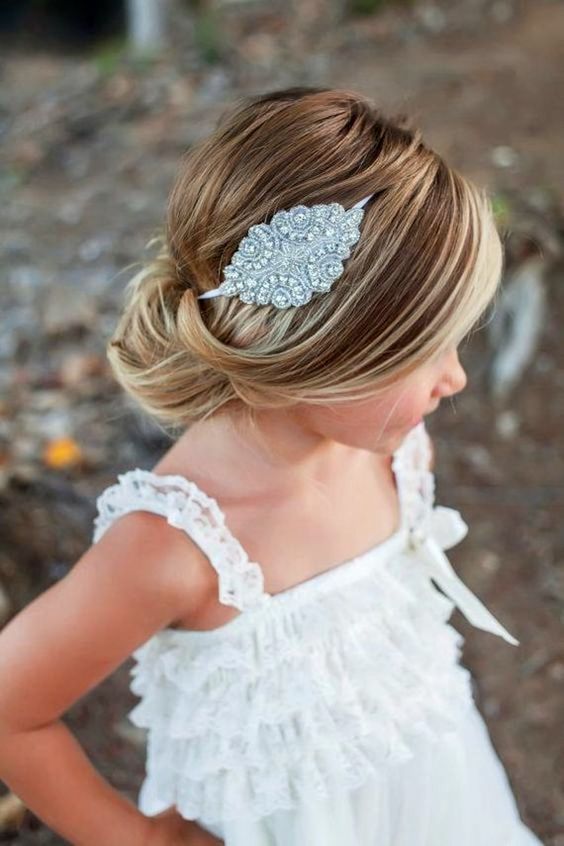 a refined flower girl hairstyle with a low bun and a bump, with a rhinestone headpiece is a chic and stylish idea