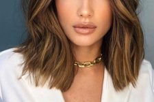 a shoulder-length hairstyle in dark brunette, with golden blonde highlights and textured volume is chic