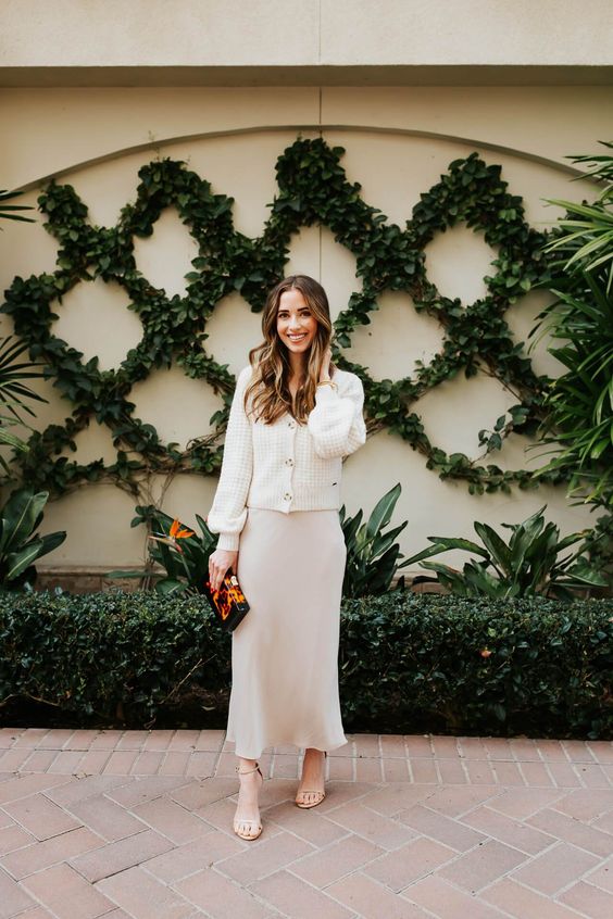 a simple and cool look with a neutral slip midi dress, a white cardigan, nude shoes and a bright bag for a winter bridal shower