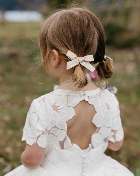 a simple and cute flower girl hairstyle with little ponytails and bows plus face-framing hair is a lovely idea
