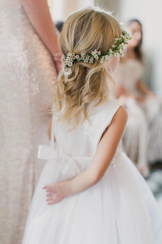 a simple wavy half updo with a bump on top and a flower crown is a cool dea for a boho flower girl look