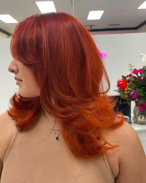 a super bright red and orange butterfly haircut on medium hair, with curtain bangs and curled ends is wow