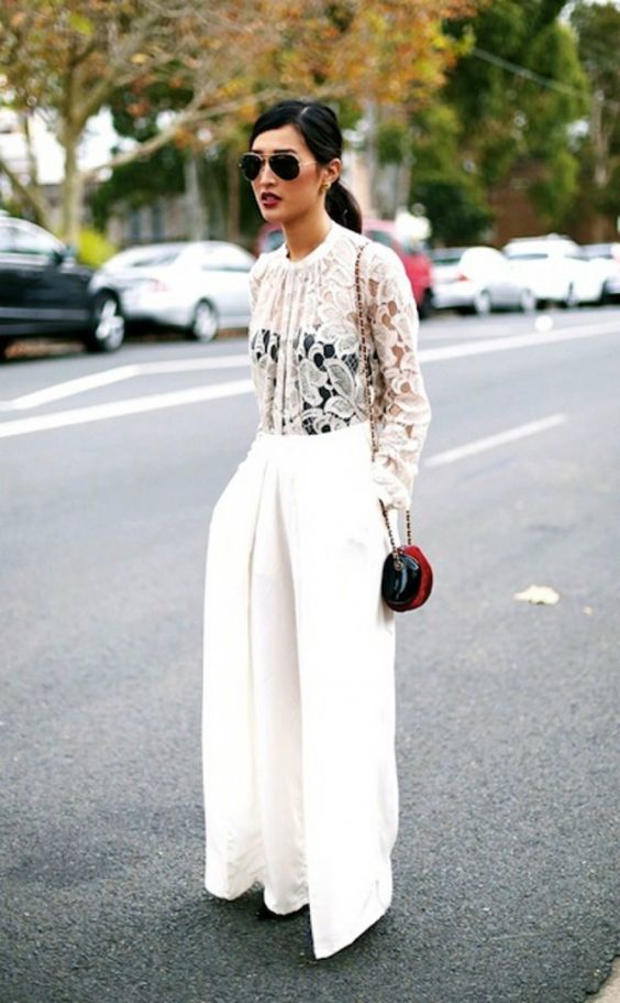 a white lace top, a black corset underneath, white wideleg pants, a small red bag for a chic winter bridal shower look