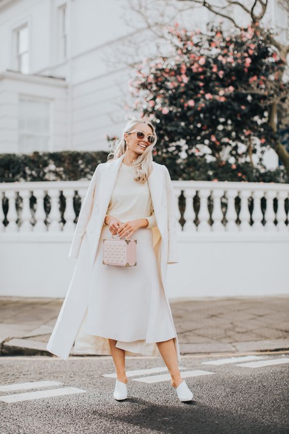 a white sweater, a midi skirt with an asymmetrical rim, white shoes, a white coat and a pink box bag