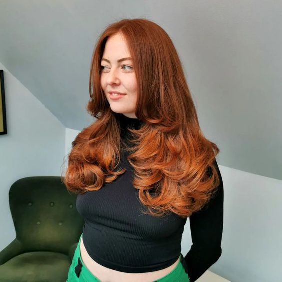 an adorable auburn to copper butterfly haircut with curled ends and a lot of volume is amazing