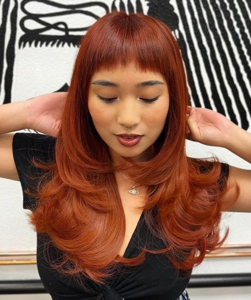 An eye catchy red butterfly haircut on long hair, with baby bangs and curled ends to make a statement