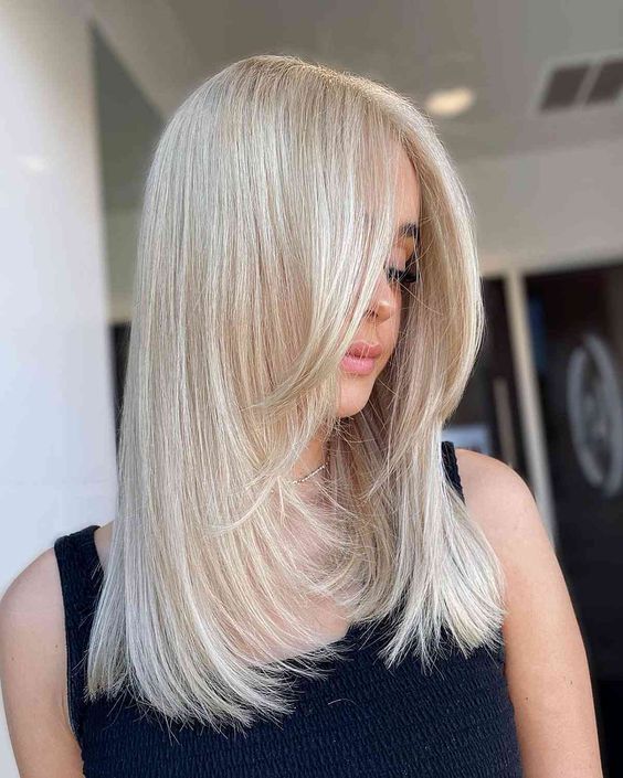 Beautiful platinum blonde medium length hair with face framing layers and curled ends is a chic hairstyle