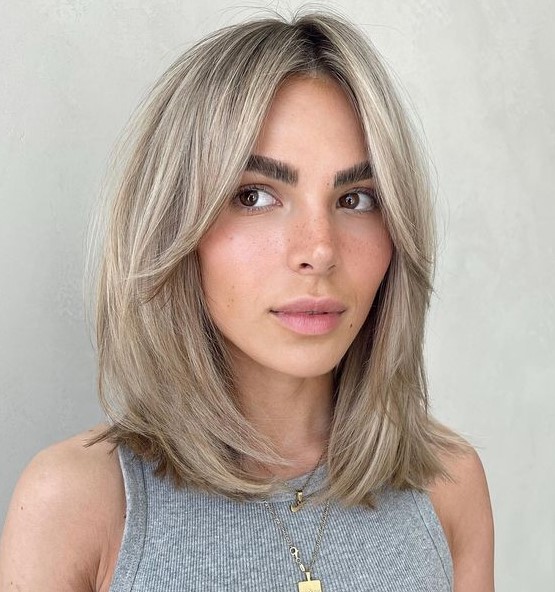 Cold blonde medium length hair with a darker root and curtain bangs is a stylish and chic idea