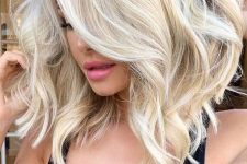 medium-length blonde hair with a darker root and waves plus a lot of volume is a stylish idea to rock