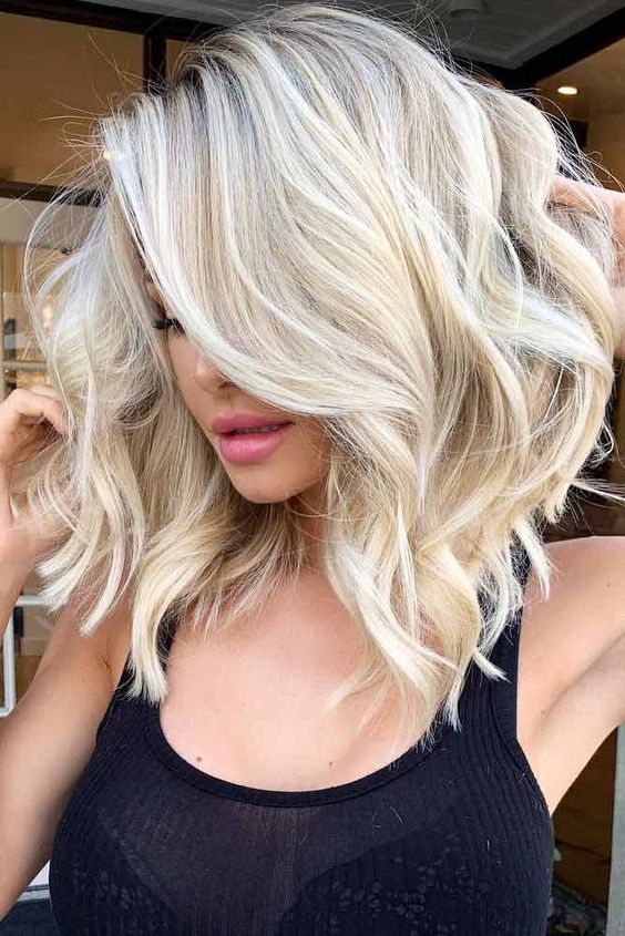 Medium length blonde hair with a darker root and waves plus a lot of volume is a stylish idea to rock