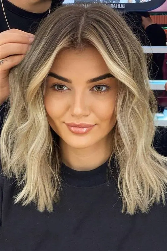 Medium length blonde hair with a shadow root and slight waves is a cool idea, it looks stylish and chic